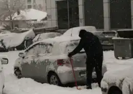 Shoveling car: Person clearing heavy snow from a parked car in winter.