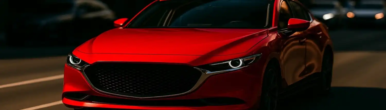red-hero-1920x1080 A bright red sedan driving through a dimly lit city street, its vivid color contrasting sharply with the darker surroundings illustrating how red automotive paint captures attention.