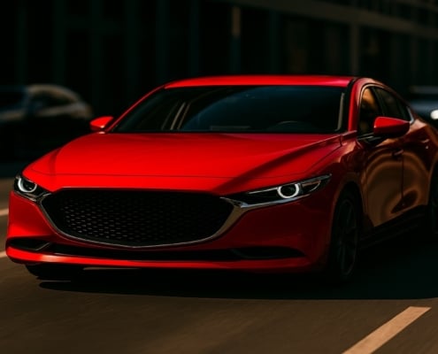 A bright red sedan driving through a dimly lit city street, its vivid color contrasting sharply with the darker surroundings illustrating how red automotive paint captures attention.