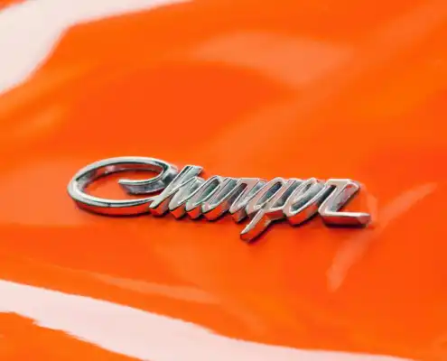 close-up-Dodge-go-mango-color Close-up of a chrome Dodge Charger emblem on a bright orange car painted in Go Mango, one of Dodge’s classic High-Impact Colors. The surface shows the vivid orange gloss associated with the Go Mango finish.